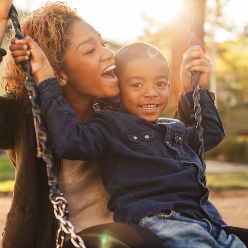 Mother and young son swinging at park on a sunny day.