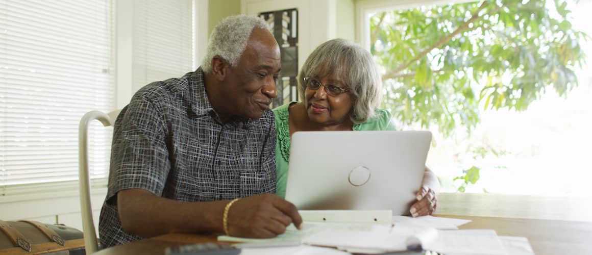 Senior African American couple at home using a gray laptop together.