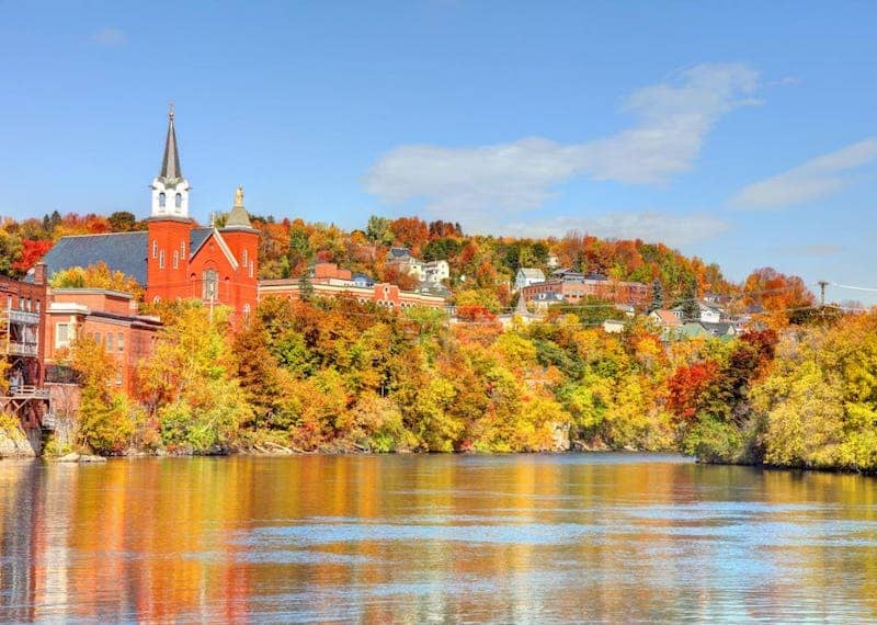 Historic buildings peeking through Fall trees on the water.