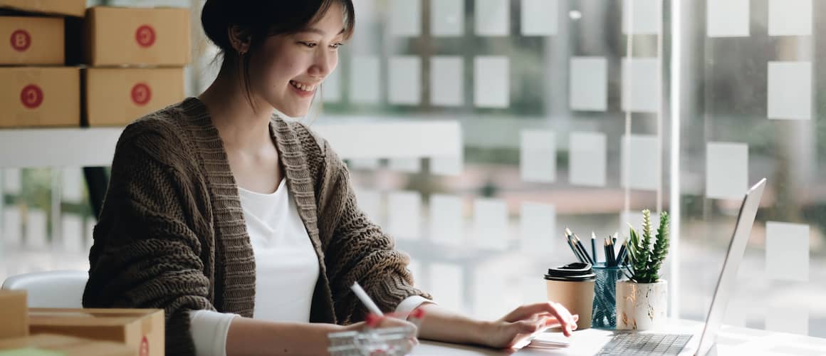 Young woman starting Small business while working at home office with boxes in background.