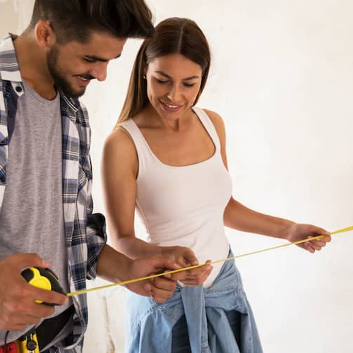 A couple holding a measuring tape possible going to renovate their house.