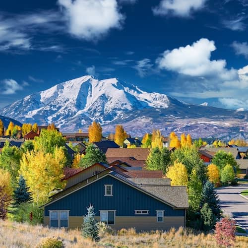Homes nestled in valley near snow capped mountain range during autumn.