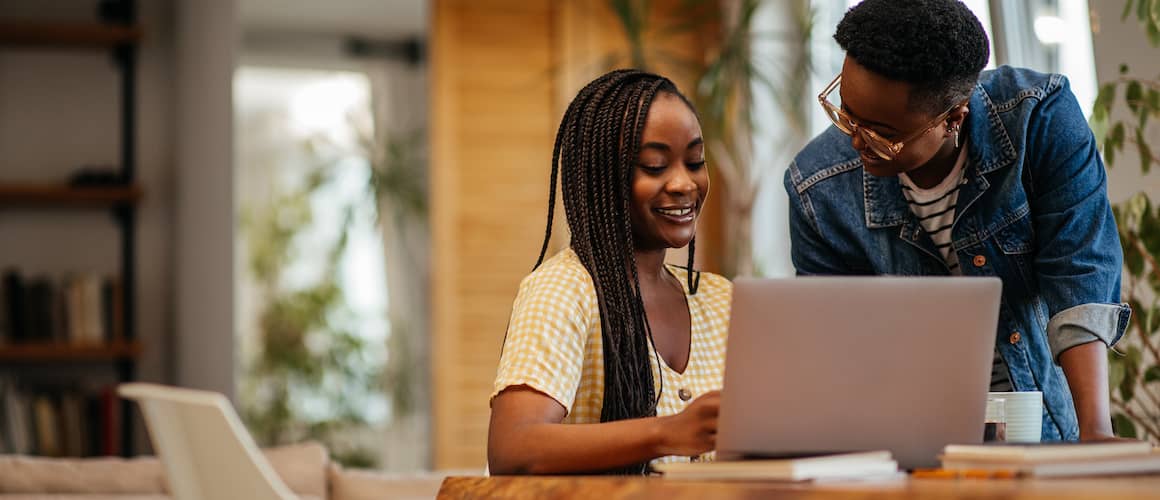 A teacher helping her student in researching student loans on laptop.