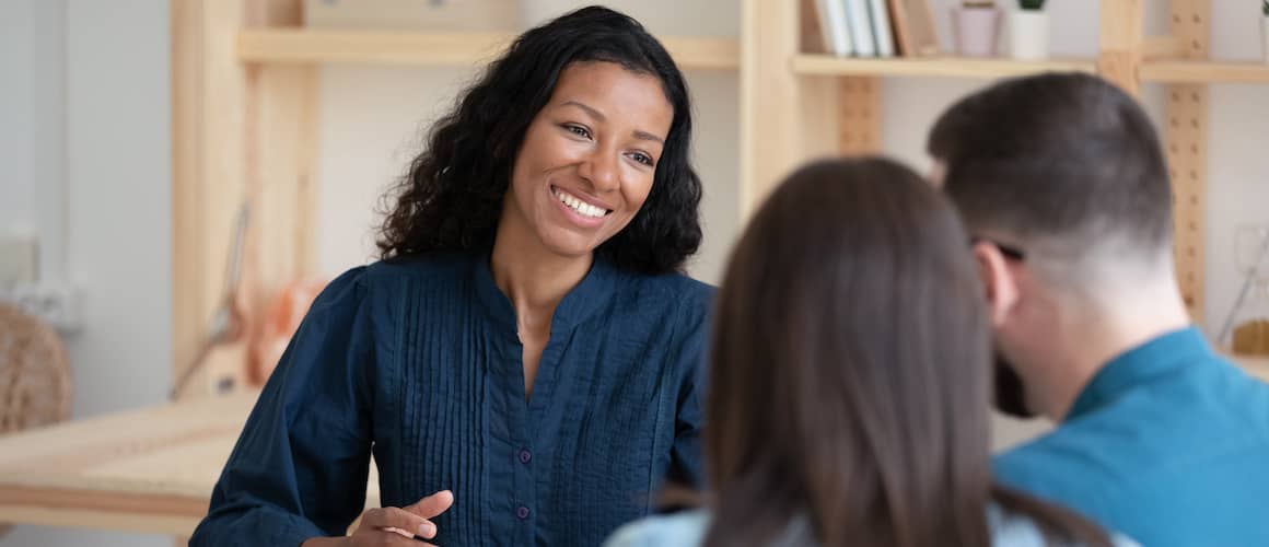 Smiling African American realtor broker manager consulting happy young couple about contract terms at meeting