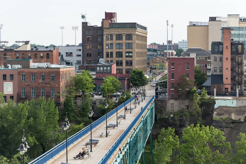 RHB Assets From IGX: A charming blue sidewalk bridge with vintage brick buildings in the background.