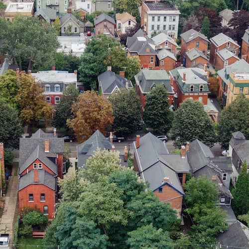 Aerial view of neighborhood with multi-story brick homes and mature green trees in Buffalo, New York.