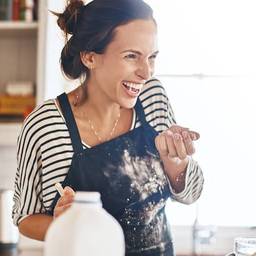 Mother and daughter laughing while baking, depicting a cheerful moment during a baking activity.