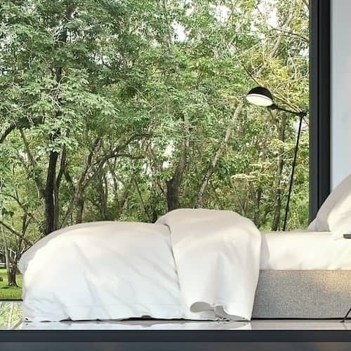 Serene bedroom overlooking trees and a comfortable bed representing a peaceful place for buying real estate or vacation home.