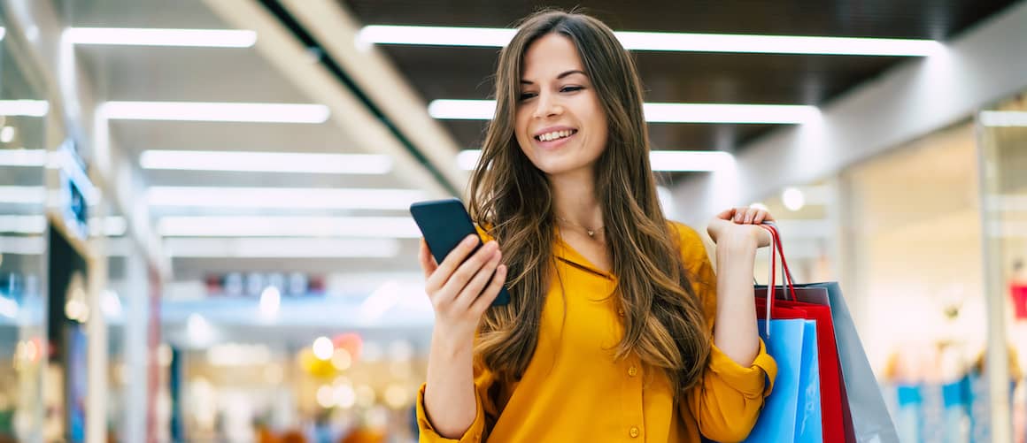 Young woman in yellow shirt checking her phone while shopping.