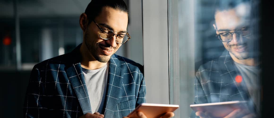 Man in thirties with business casual look smiling as he views information on his tablet.