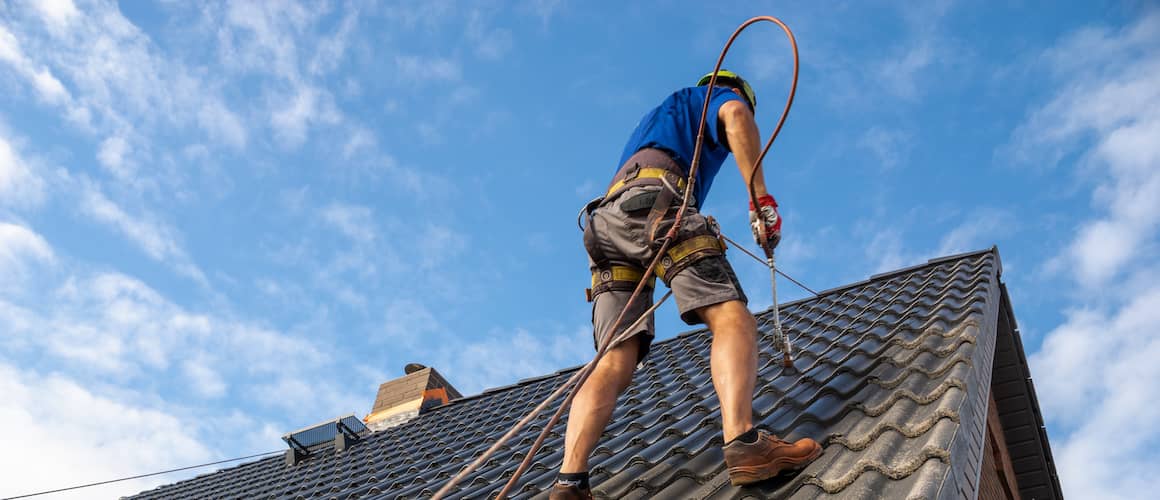 A worker painting a roof, likely involved in maintenance or renovation work on a building.