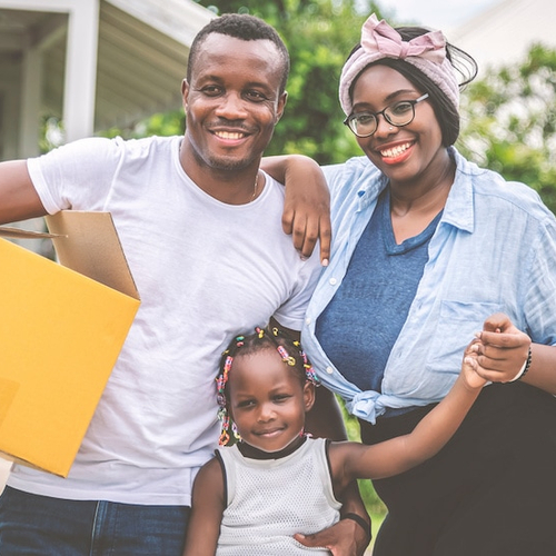 A family in the process of moving into a new home, carrying boxes and belongings.