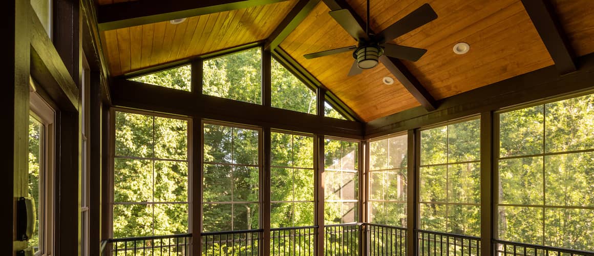 Screened in windowed sun room porch with vaulted roof overlooking wooded yard.