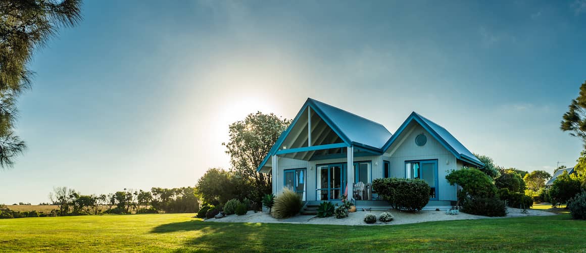 Small, white house with blue roof on large lot.