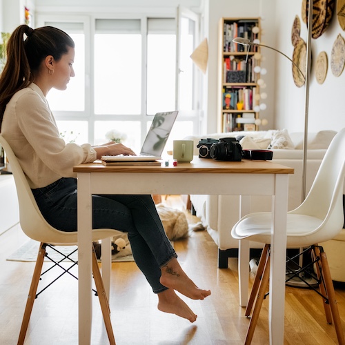 Young woman at desk in studio apartment searching for a home on her laptop.