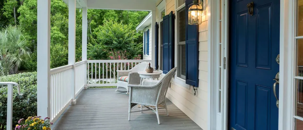 Front porch of a home with white wicker chairs and a blue front door.