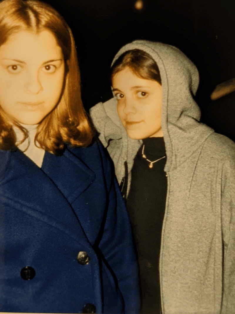 Two young girls looking at the camera, one with her sweatshirt hood up. 