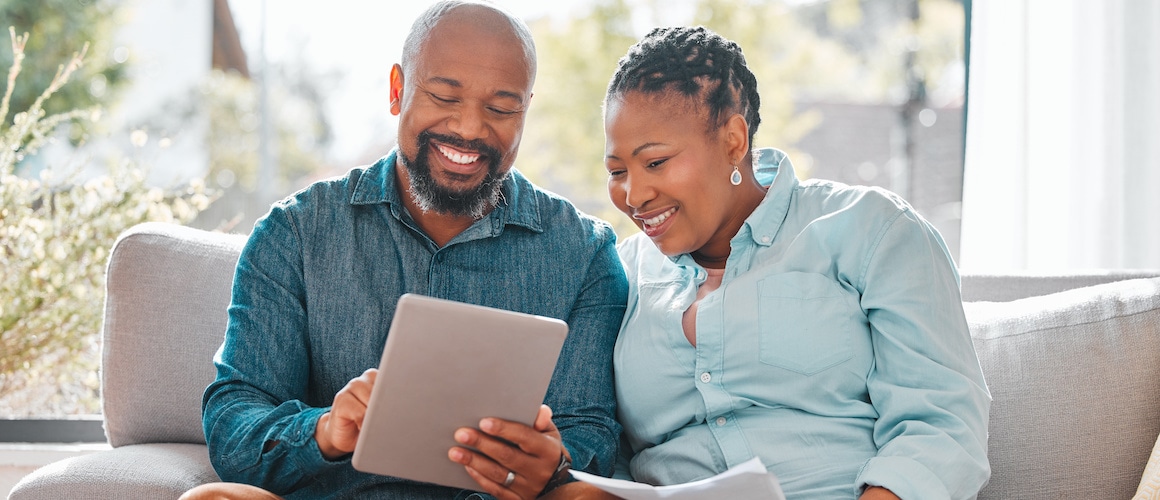A mature couple looking through their bills while using a digital tablet, possibly managing finances or household expenses.