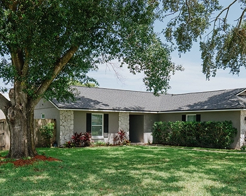 Ranch-style home with stone features and two large trees out front.