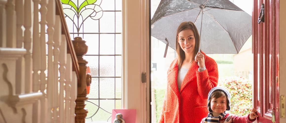 Loving mother standing with her smiling young son in the sunny doorway of their home.