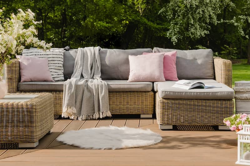 Pastel pink pillows on grey sofa in green garden with wooden terrace