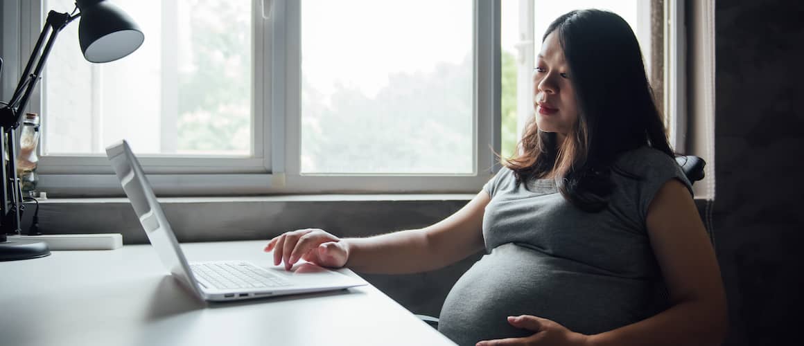 A pregnant Asian woman browsing or working on a computer, possibly researching or organizing information online.