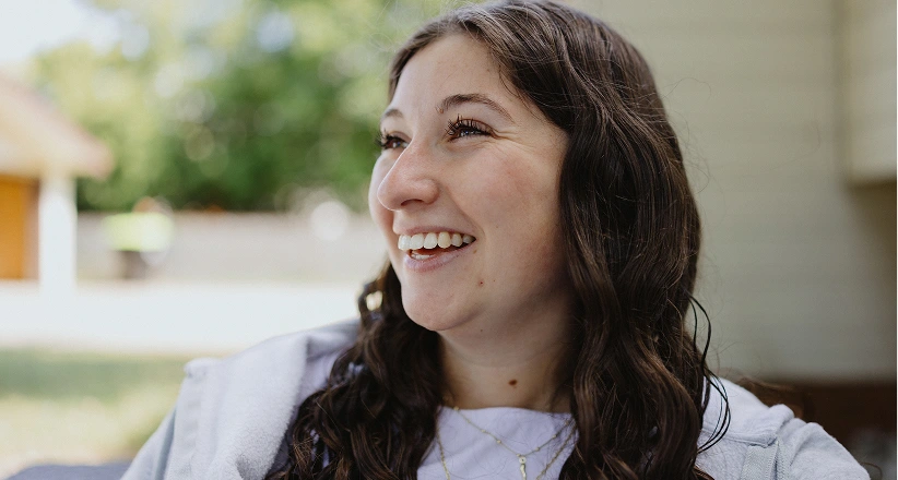 A person in a yellow top is in a hallway or corridor, with other people visible in the background. Their face is blurred for privacy.
