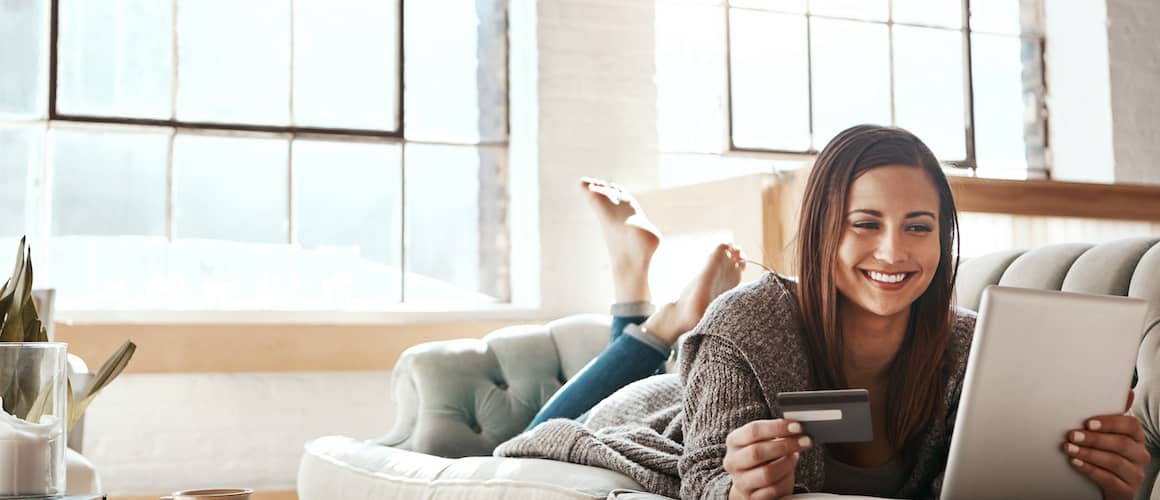 Woman checking her credit on her tablet, relaxing on her couch and smiling.