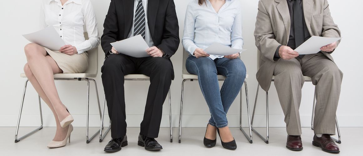 Line of people sitting down in chairs in a waiting room for interviews.