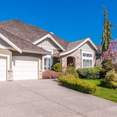 Ranch-style home with tan siding, stone accents and a beautifully manicured lawn.