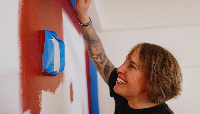 Person with short hair and tattoos on arm smiling while painting wall red.