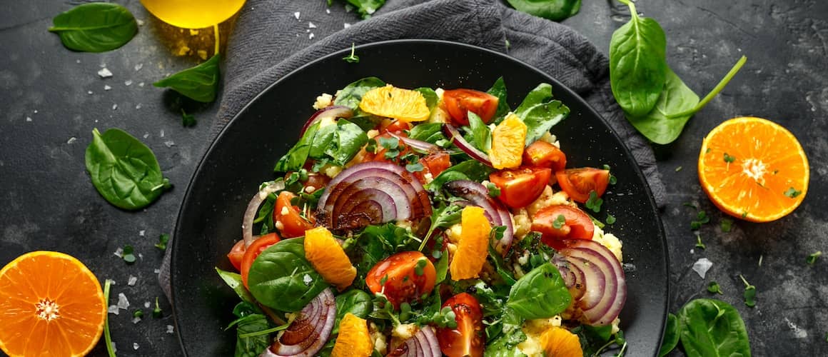 A colorful vegetable millet salad in a black bowl.