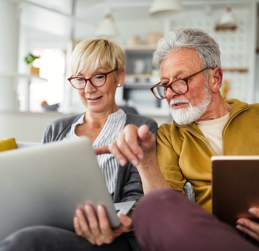 Senior couple sitting on a couch at home with a laptop and book.