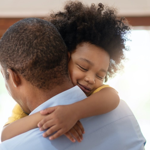 A father hugging his young son, in their home.