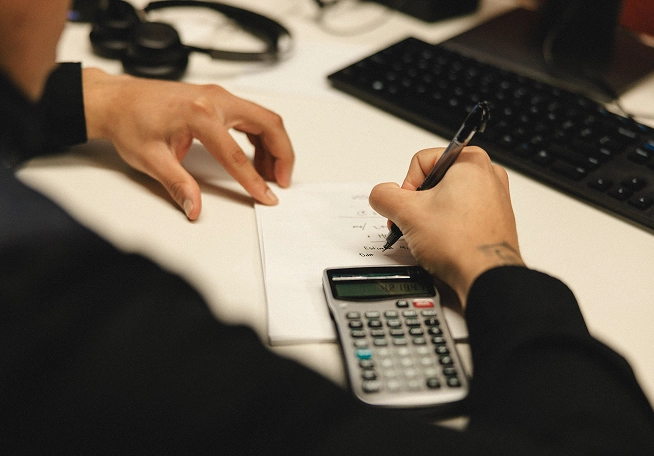 A man doing math by hand, alternating between a calculator and his notepad.