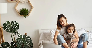 Una madre y una hija blancas sentadas en un sofá y mirando una computadora portátil.