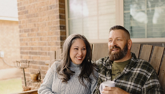 Couple smiling, sitting on front porch with coffee.