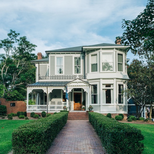 Historic Mississippi home with white and grey paint and a green hedge-lined walkway.