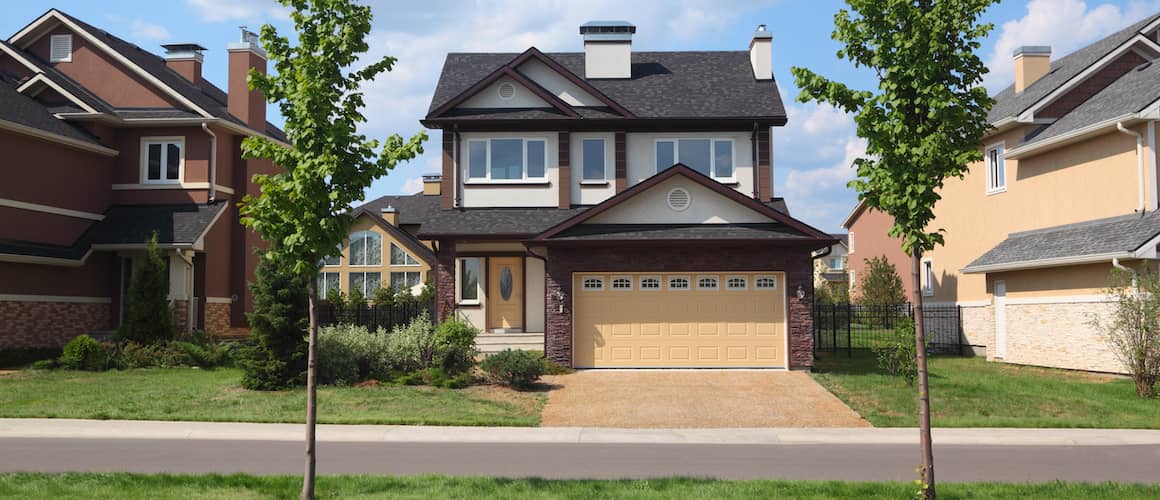 Two-story brick cottage on sunny street.