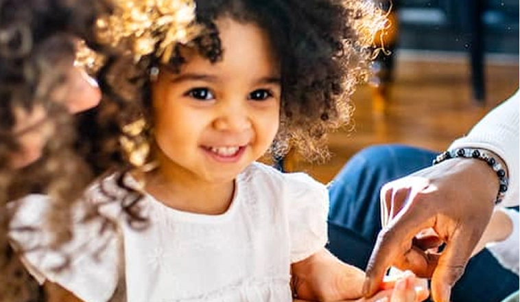 A toddler standing between her parents, who are gently helping with an activity.