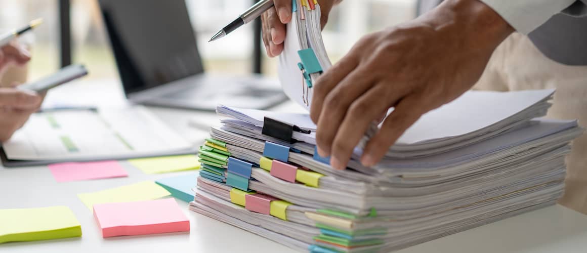 Man stacking piles of binder clipped paperwork on desk.