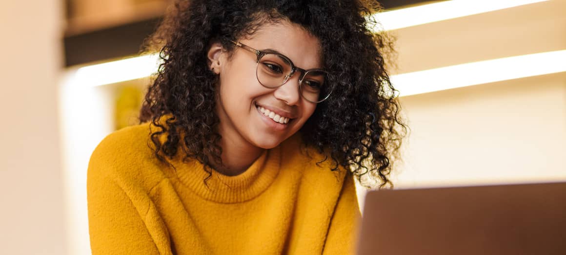 A woman in a sweater looking at a laptop, possibly working or engaging in online activities.