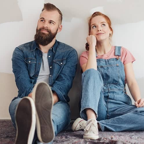 A young couple sitting on the floor side by side, potentially discussing home-related decisions or planning.