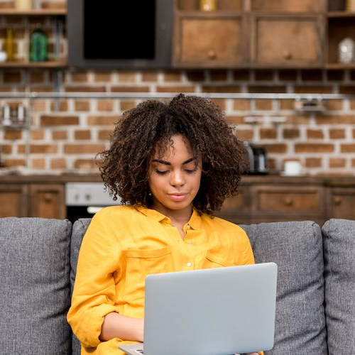 Woman working with a laptop on a couch, potentially managing finances or exploring real estate options online.