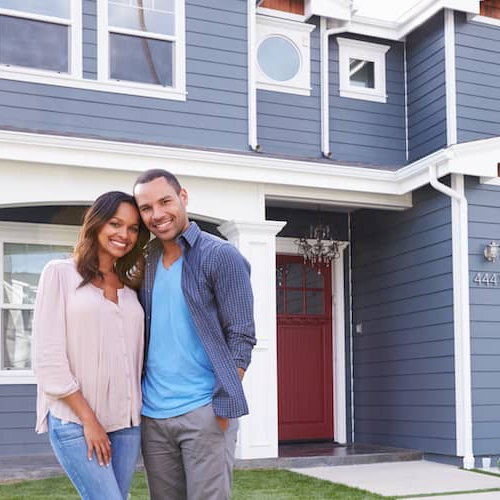 Couple standing in front of their new home, expressing excitement and happiness.