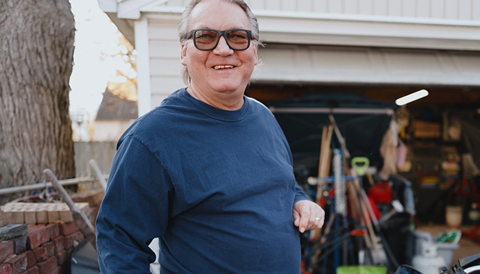Man in orange glasses smiling next to his motorcycle.