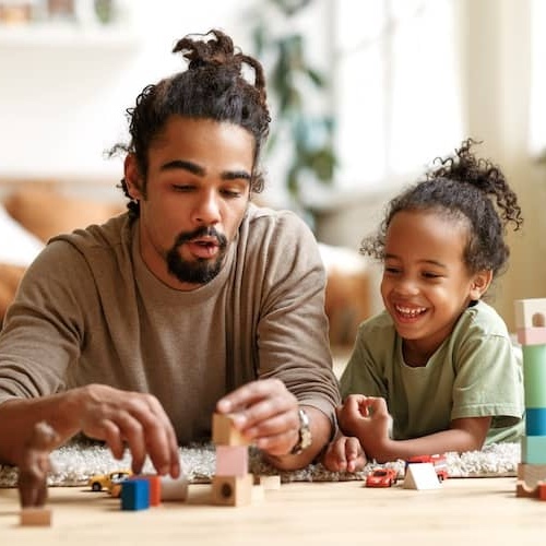 Father and son playing with wooden blocks together on floor of living room.