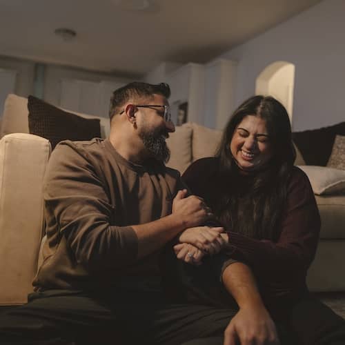 Couple holding each other on floor near couch and laughing.