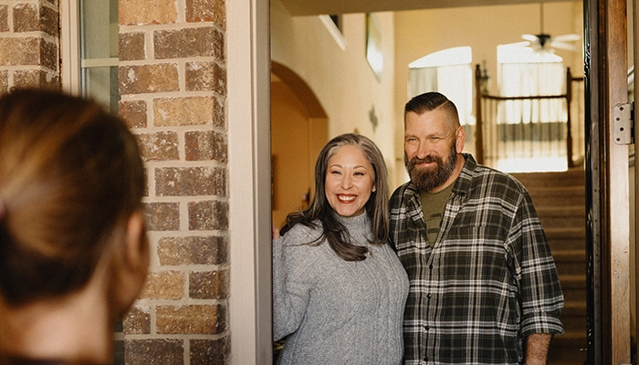 Couple standing in doorway smiling at person partially out of frame.