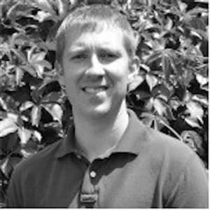 Picture of a man in black and white against a leafy background.